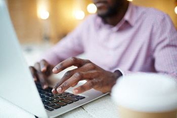 African American man wearing a pink/purple shirt on laptop typing.